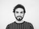 Retrato en blanco y negro de un hombre joven con barba y pelo rizado que mira serio a la cámara
