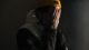 Joven con gorro amarillo que se cubre la cara con las manos, en penumbra