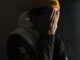Joven con gorro amarillo que se cubre la cara con las manos, en penumbra