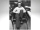 Albert Ellis sonriente, sentado en un sillón con las piernas cruzadas, foto en blanco y negro