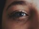 Primer plano del ojo azul de una mujer con salpicaduras de pintura negra en la piel alrededor del párpado