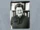 Retrato en blanco y negro de Mary Ainsworth sonriente, con gafas, delante de una estantería con libros