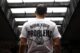 Hombre joven de espaldas con una camiseta blanca que dice «Burn your problems», bajo un puente