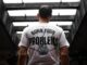 Hombre joven de espaldas con una camiseta blanca que dice «Burn your problems», bajo un puente