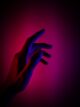 Mano extendida iluminada con luz roja y azul sobre un fondo oscuro en tonos magenta