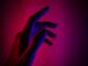 Mano extendida iluminada con luz roja y azul sobre un fondo oscuro en tonos magenta