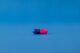 Cápsula de medicamento azul y rosa tumbada sobre un fondo azul liso
