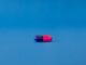 Cápsula de medicamento azul y rosa tumbada sobre un fondo azul liso