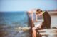 Joven sentado a solas en un muelle frente al mar, leyendo un libro