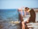 Joven sentado a solas en un muelle frente al mar, leyendo un libro