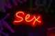 Letrero de neón rojo y amarillo con la palabra «Sex» sobre una pared oscura