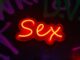 Letrero de neón rojo y amarillo con la palabra «Sex» sobre una pared oscura