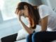 Mujer sentada en un sofá con la cabeza apoyada en la mano y expresión de agotamiento