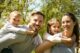 Familia sonriente al aire libre: el padre y la madre llevan a caballito a un niño y a una niña