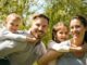 Familia sonriente al aire libre: el padre y la madre llevan a caballito a un niño y a una niña
