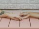 Dos manos que se toman sobre una mesa de madera rosada, una de ellas con un tatuaje en el brazo