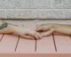 Dos manos que se toman sobre una mesa de madera rosada, una de ellas con un tatuaje en el brazo