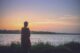 Silueta de una mujer de pie sola a la orilla de un lago al atardecer