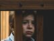 Niño pequeño con expresión triste se asoma entre los barrotes de madera de una barandilla