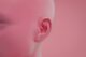 Primer plano de una oreja en una cabeza rosada sin pelo, sobre fondo rosa