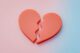 Corazón rojo partido en dos piezas sobre un fondo degradado rosa y celeste