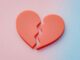 Corazón rojo partido en dos piezas sobre un fondo degradado rosa y celeste