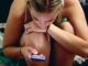 Mujer joven sentada abrazada a sus rodillas mientras mira el móvil