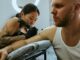 Tatuadora con guantes negros tatúa el brazo de un hombre con camiseta blanca de tirantes