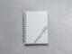 Cuaderno de espiral cerrado con un bolígrafo encima, sobre una superficie gris
