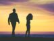Siluetas de un hombre y una mujer caminando por separado a contraluz frente al mar al atardecer