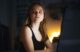 Mujer joven frente a una pantalla en una habitación oscura mira de reojo con expresión de sospecha
