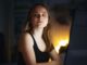 Mujer joven frente a una pantalla en una habitación oscura mira de reojo con expresión de sospecha