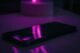 Teléfono móvil apoyado sobre una mesa, iluminado con luz violeta en la oscuridad