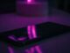 Teléfono móvil apoyado sobre una mesa, iluminado con luz violeta en la oscuridad