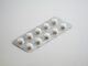 Blíster de pastillas blancas redondas sobre una superficie gris claro