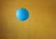 Globo azul a punto de ser pinchado por un alfiler sobre un fondo mostaza