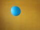 Globo azul a punto de ser pinchado por un alfiler sobre un fondo mostaza