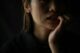 Mujer en penumbra con una lágrima en la mejilla y la mano junto a la boca