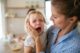 Niña pequeña llorando a gritos en brazos de su madre, que la mira e intenta calmarla