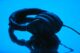 Auriculares negros sobre una superficie azul brillante que los refleja