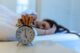 Mujer dormida en la cama que estira el brazo hacia un despertador sonando en la mesita