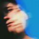 Retrato movido de una persona cuyo rostro aparece desenfocado y desdoblado sobre un fondo azul