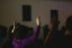 Personas de espaldas con los brazos en alto durante una celebración religiosa en penumbra