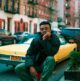 Joven sentado en la calle con la mano en la barbilla, aburrido, junto a un taxi amarillo en Nueva York