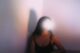 Mujer de pelo largo sentada junto a una pared, con la cara oculta por un destello de luz blanca