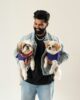 Hombre sonriente con chaqueta vaquera sostiene en brazos a dos perritos pequeños vestidos con suéteres