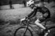 Ciclista de montaña con casco que pedalea por un camino de tierra, en blanco y negro