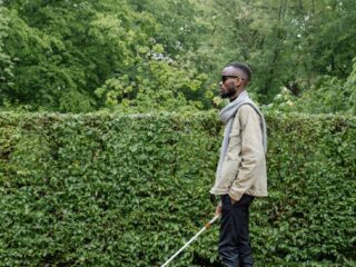 man in beige jacket waling with a white cane