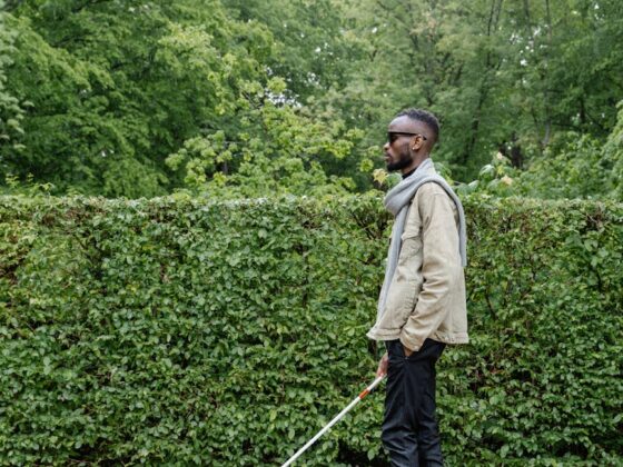 man in beige jacket waling with a white cane