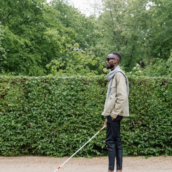 man in beige jacket waling with a white cane